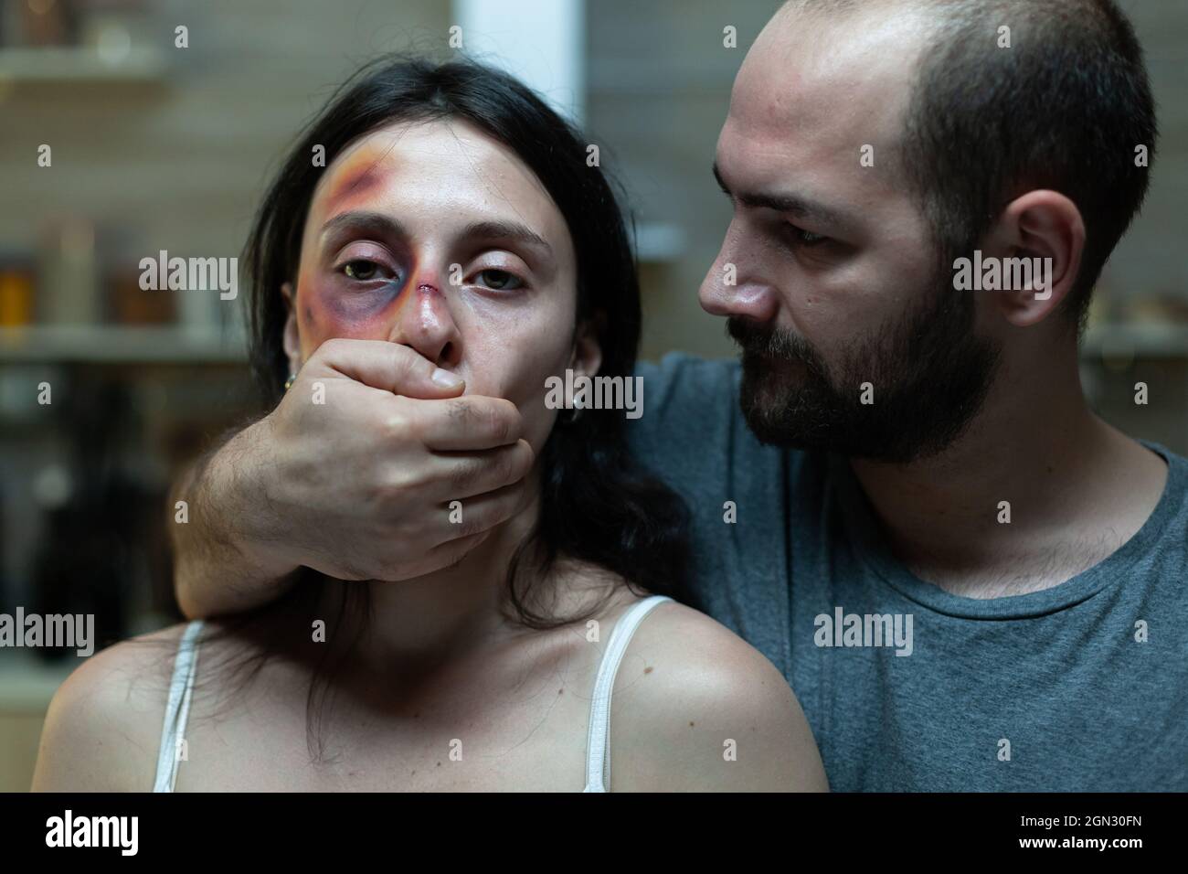 Criminal adult abusing afraid woman with bruises on face while holding hand on mouth for silence. Close up of couple with domestic issues and anger problems. Caucasian people violence Stock Photo