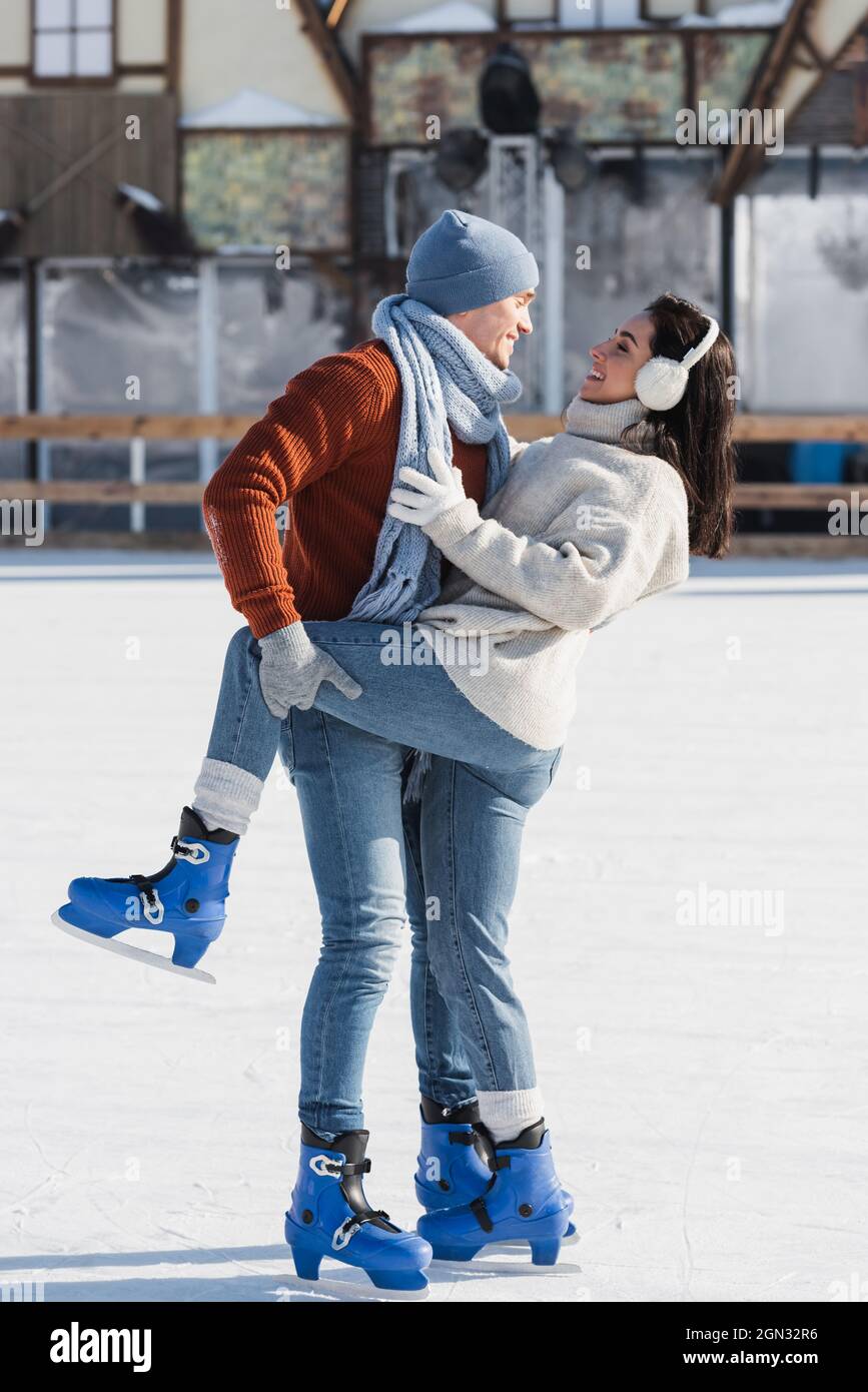 full length of cheerful man lifting leg of happy girlfriend on ice rink Stock Photo