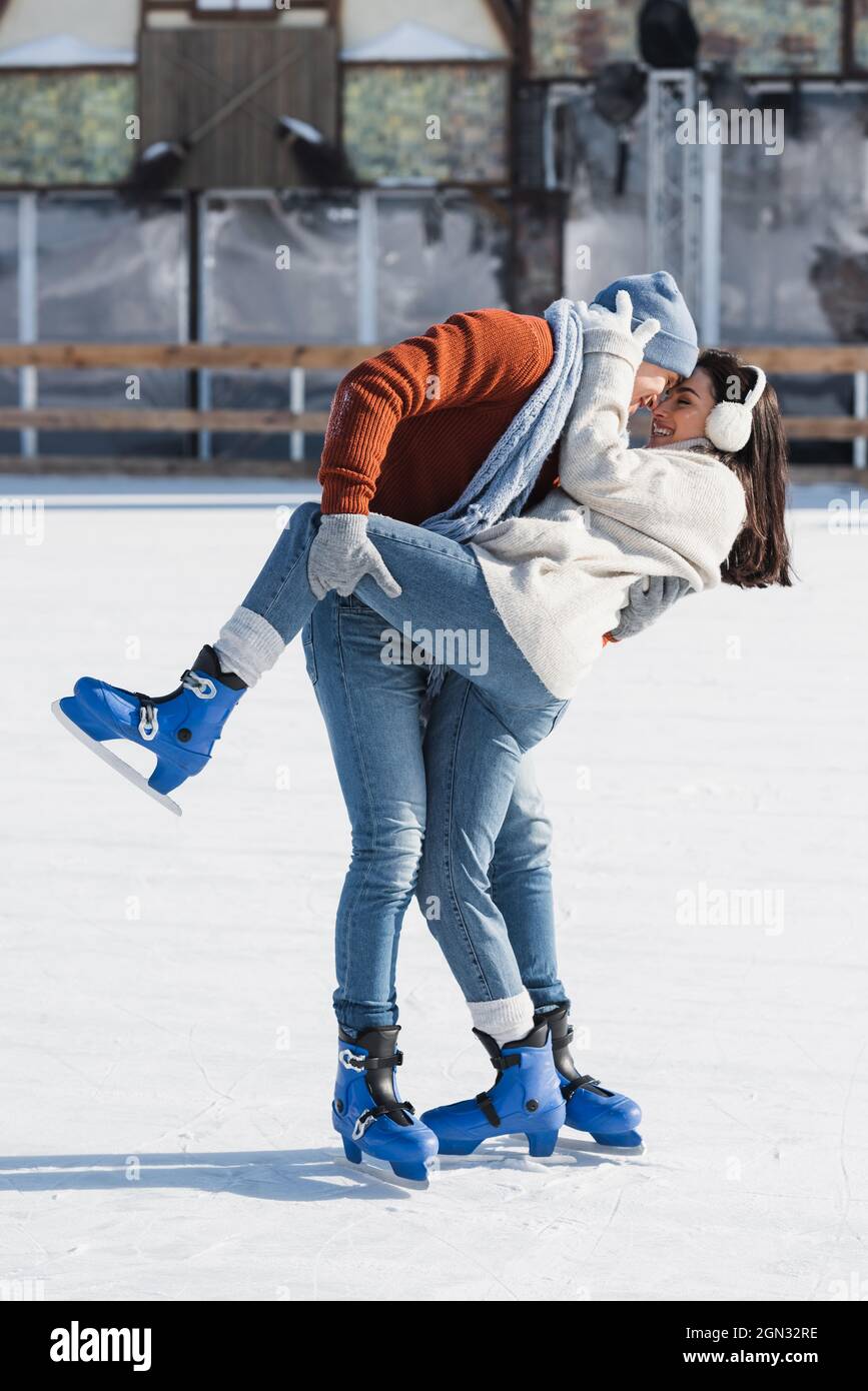 full length of smiling man lifting leg of happy girlfriend on ice rink Stock Photo