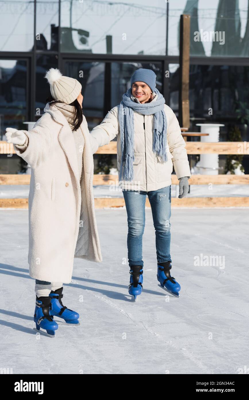 full length of young and happy couple holding hands while skating on