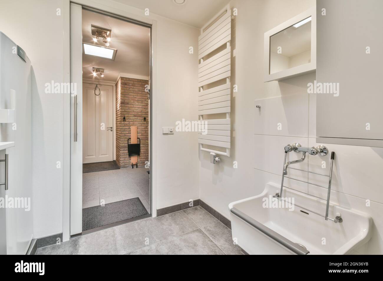 Contemporary bathroom with heated towel rail and washbasin against entrance door under lamp in house Stock Photo