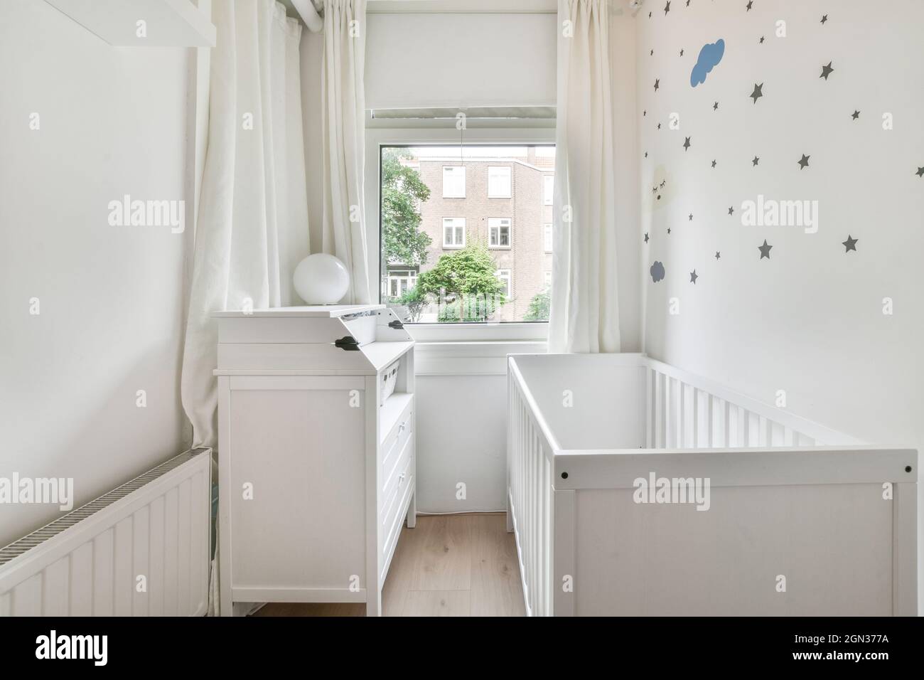 Small wooden baby cot placed near window in bedroom with minimalistic interior in daytime Stock Photo