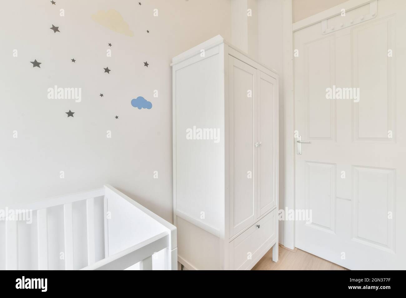 Small wooden baby cot placed near wardrobe in bedroom with minimalistic interior in daytime Stock Photo