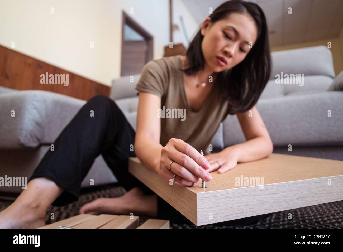 Inching Through Table Young ethnic female inserting screw into tabletop while assembling ...