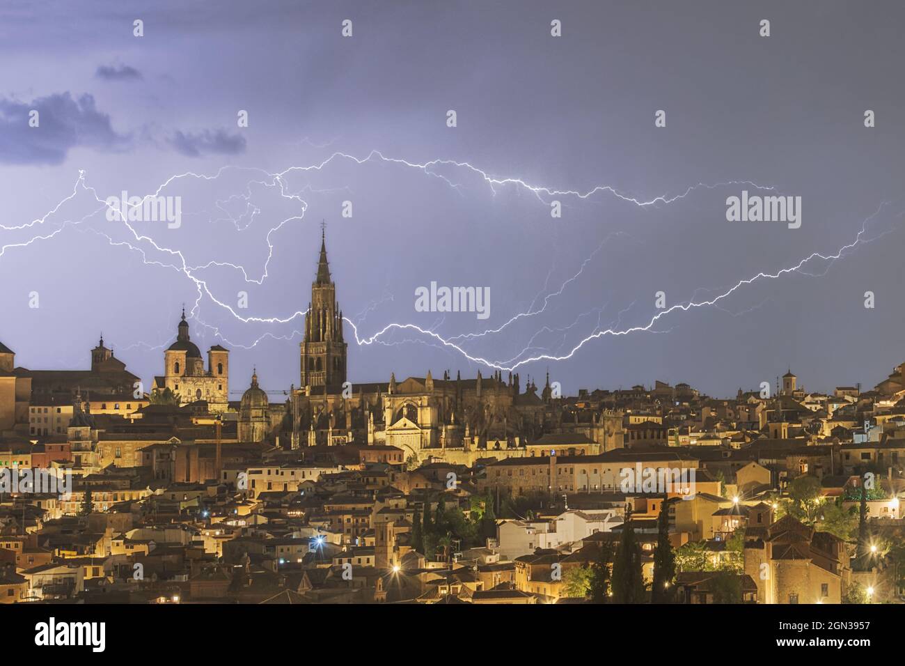 Cityscape of Toledo with high aged tower under cloudy sky with lightning during thunderstorm in night time Stock Photo