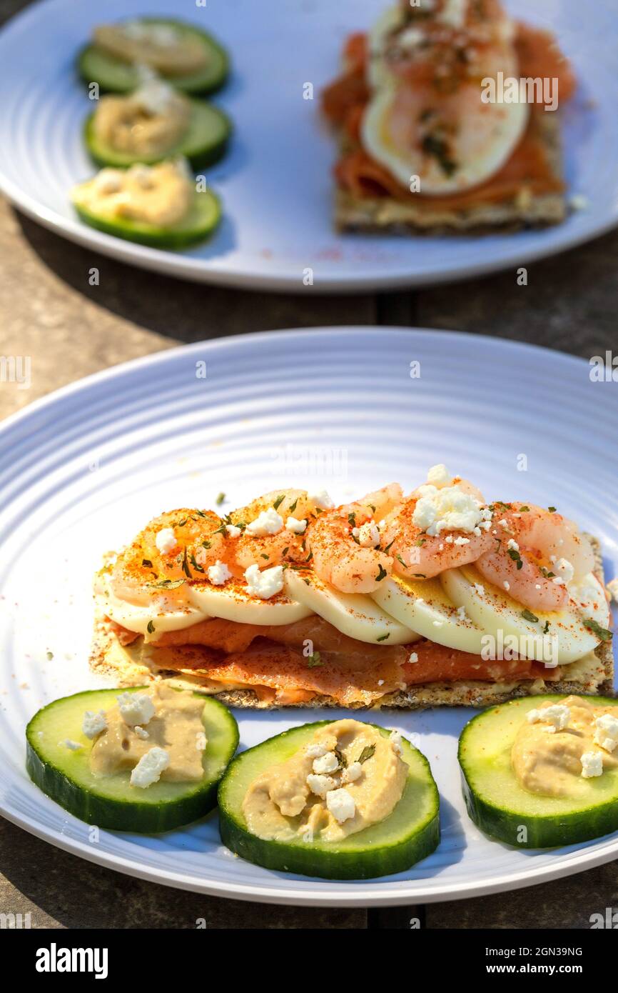 Scandinavian Style Open Sandwich Rye Crisp Bread Smoked Salmon Sliced Boiled Egg Shrimp Prawns Feta Cheese And Paprika Cucumber Slices With Hummus Stock Photo