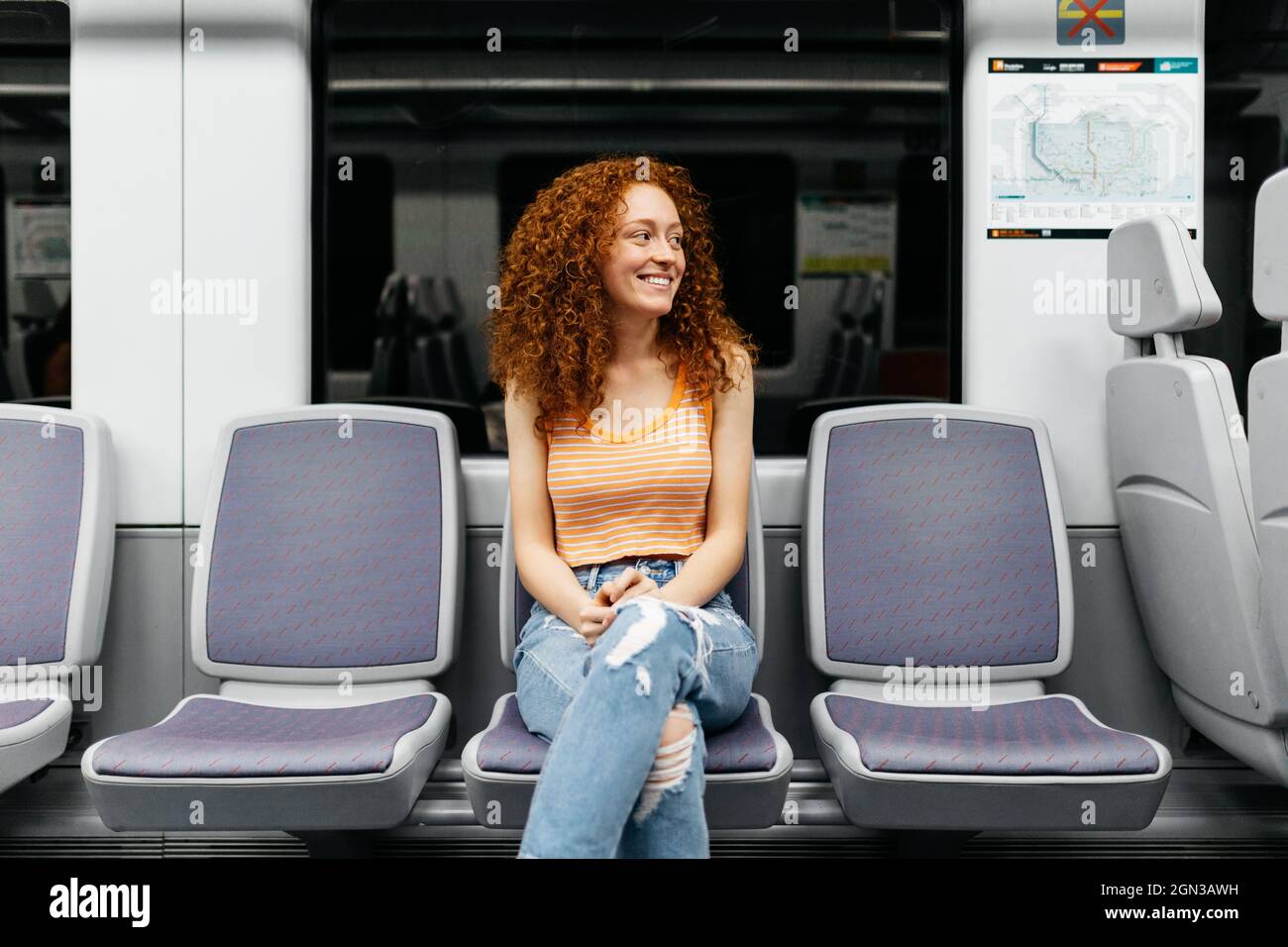 Content young Woman in ripped jeans with curly red hair looking away on  seat while travelling by train Stock Photo - Alamy