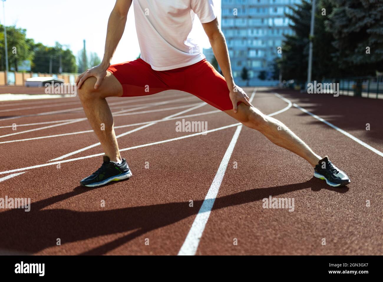 Young Caucasian sportive man, male athlete, runner practicing alone at public stadium, sport court or running track outdoors. Summer sport games. Stock Photo