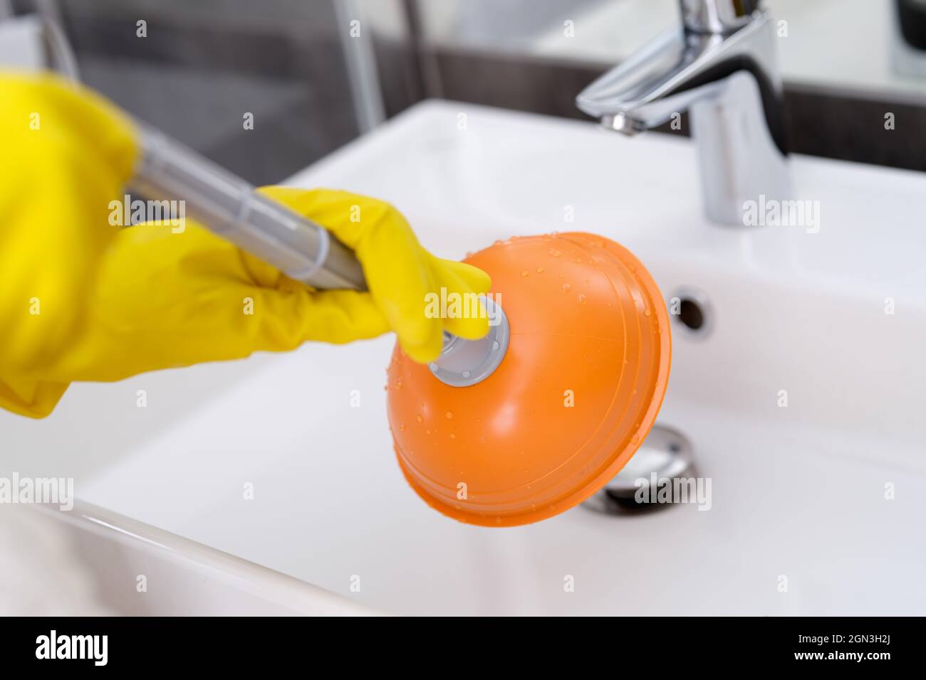 Plumber with rubber gloves cleaning sink with plunger in bathroom