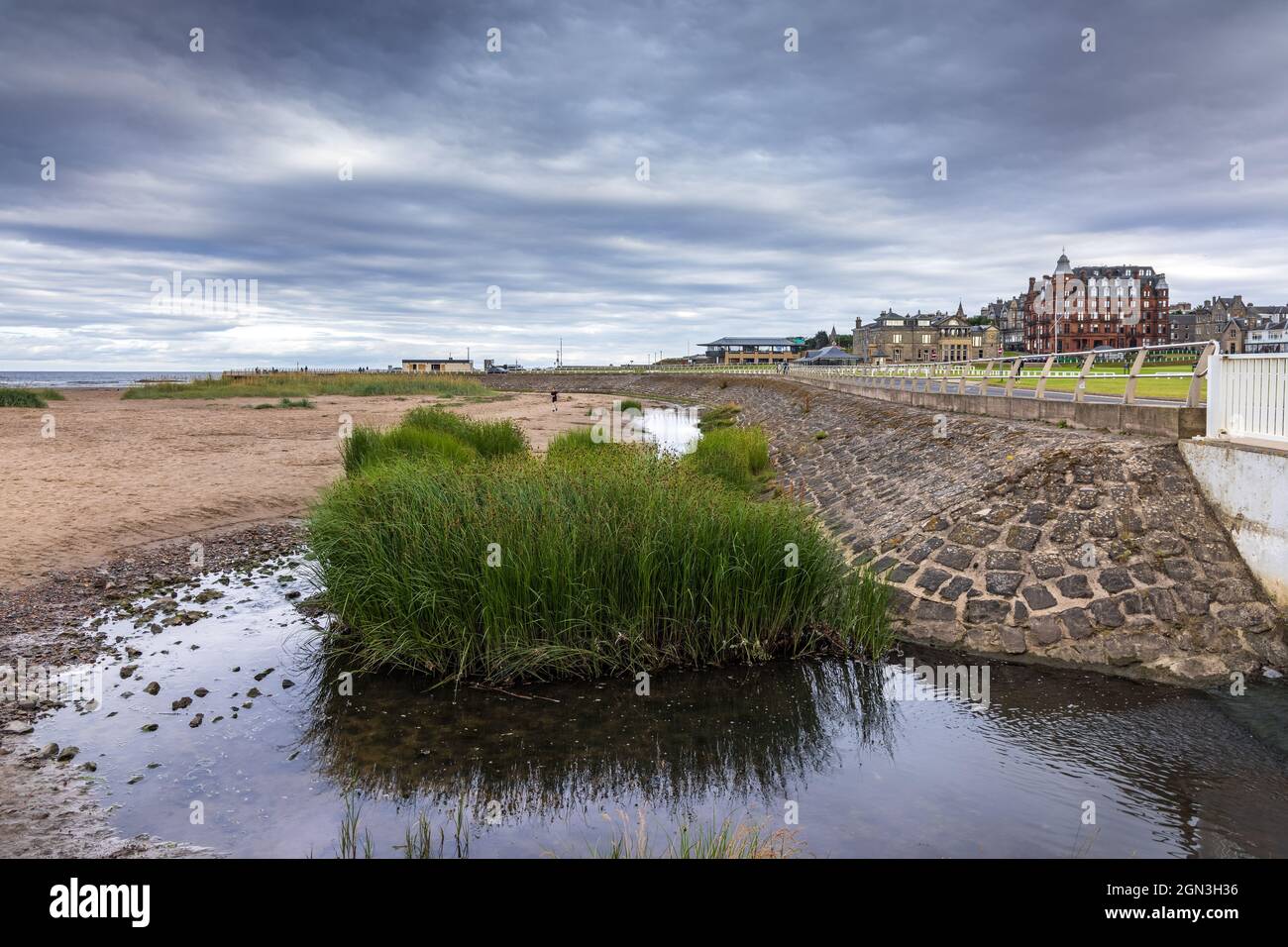 West Sands Embankment, St Andrews, with the Swilcan Burn flowing from the Old Course into the sea and the Royal and Ancient Golf Club clubhouse beyond Stock Photo