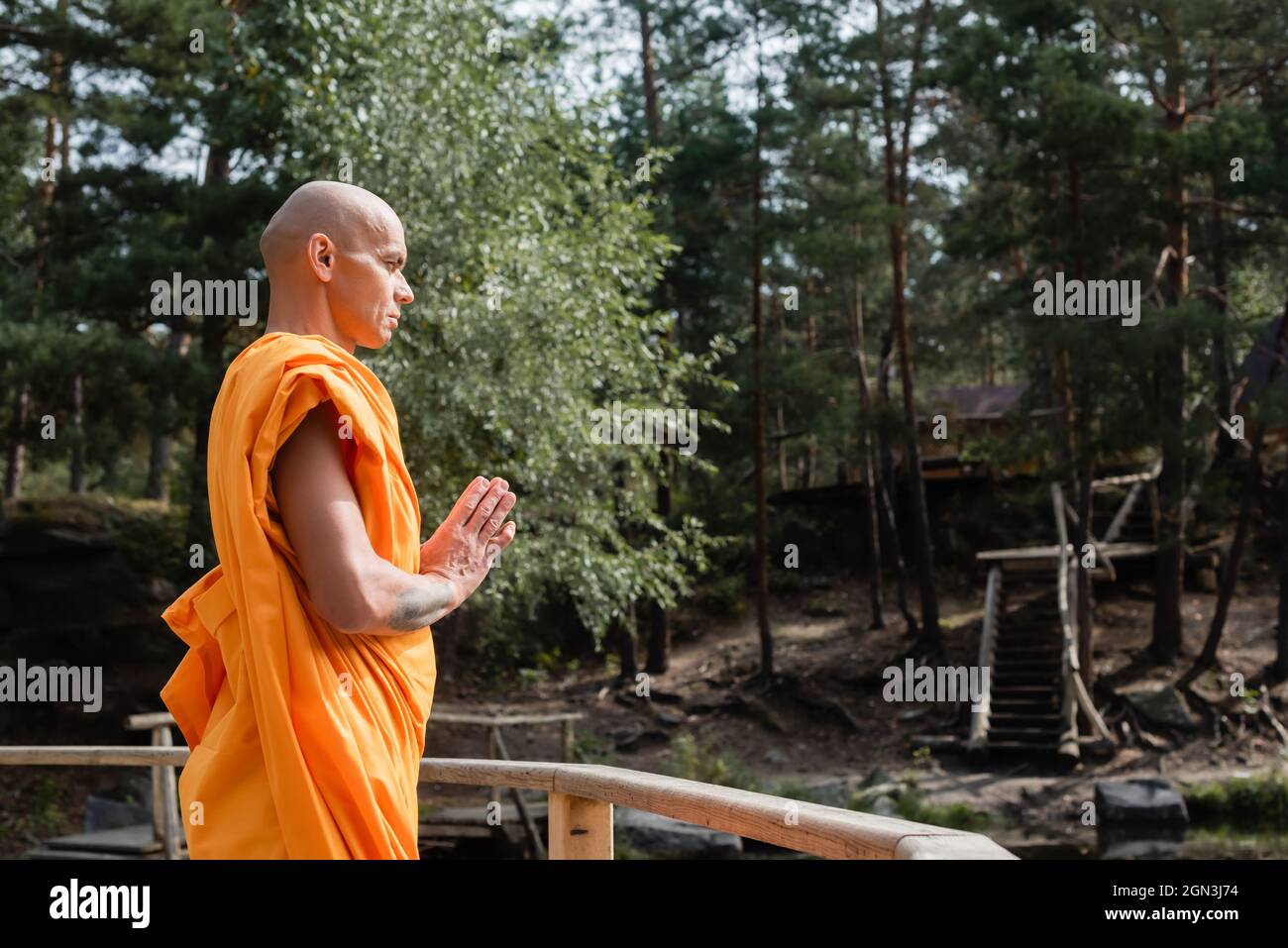 side view of buddhist meditating with praying hands near wooden fence ...