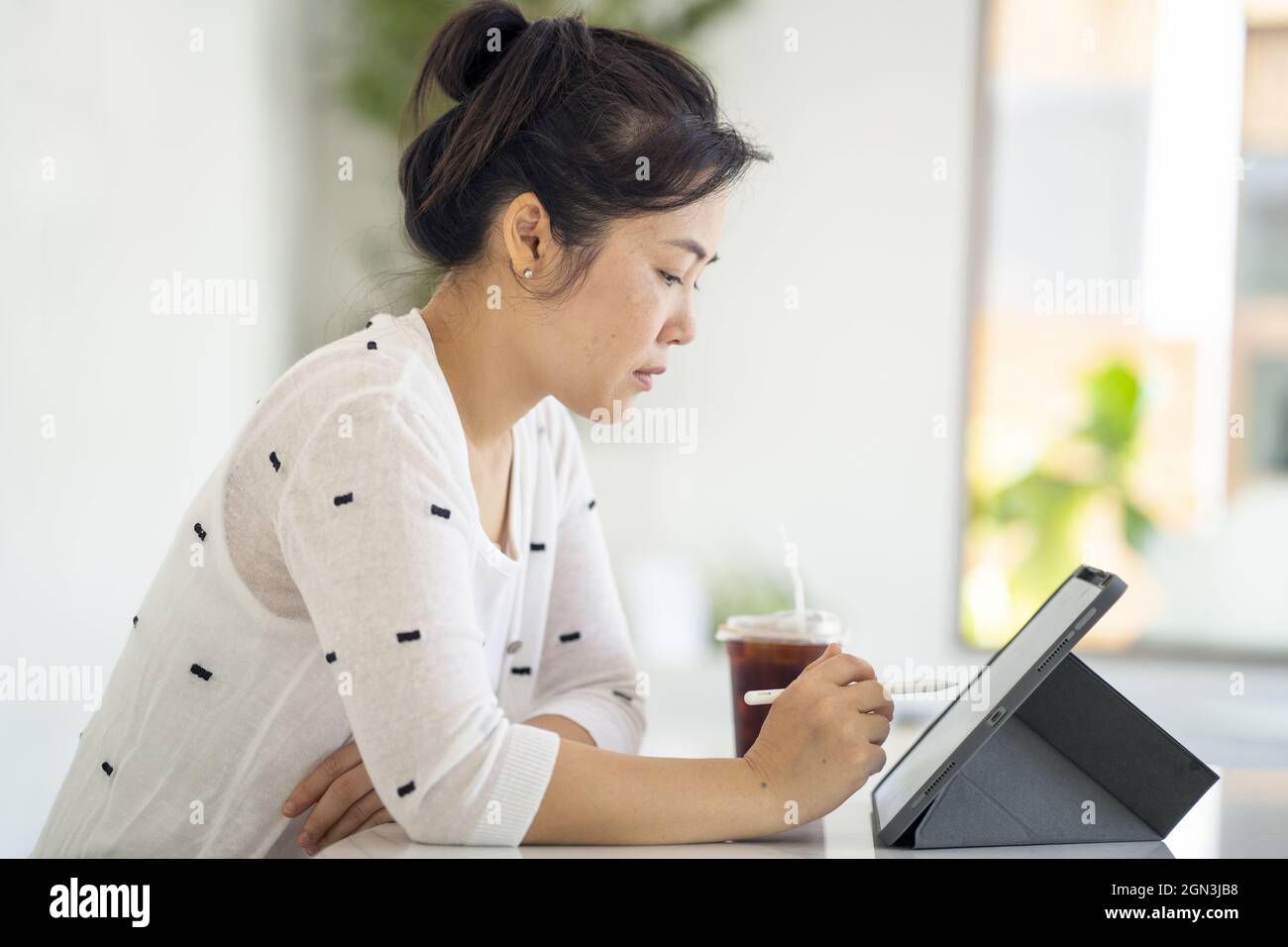 Asian female working on her tablet and drinking coffee Stock Photo