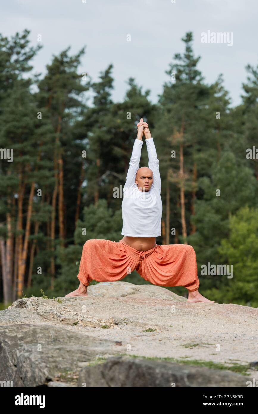 full length view of buddhist in sweatshirt and harem pants practicing yoga  in one legged tree pose Stock Photo - Alamy