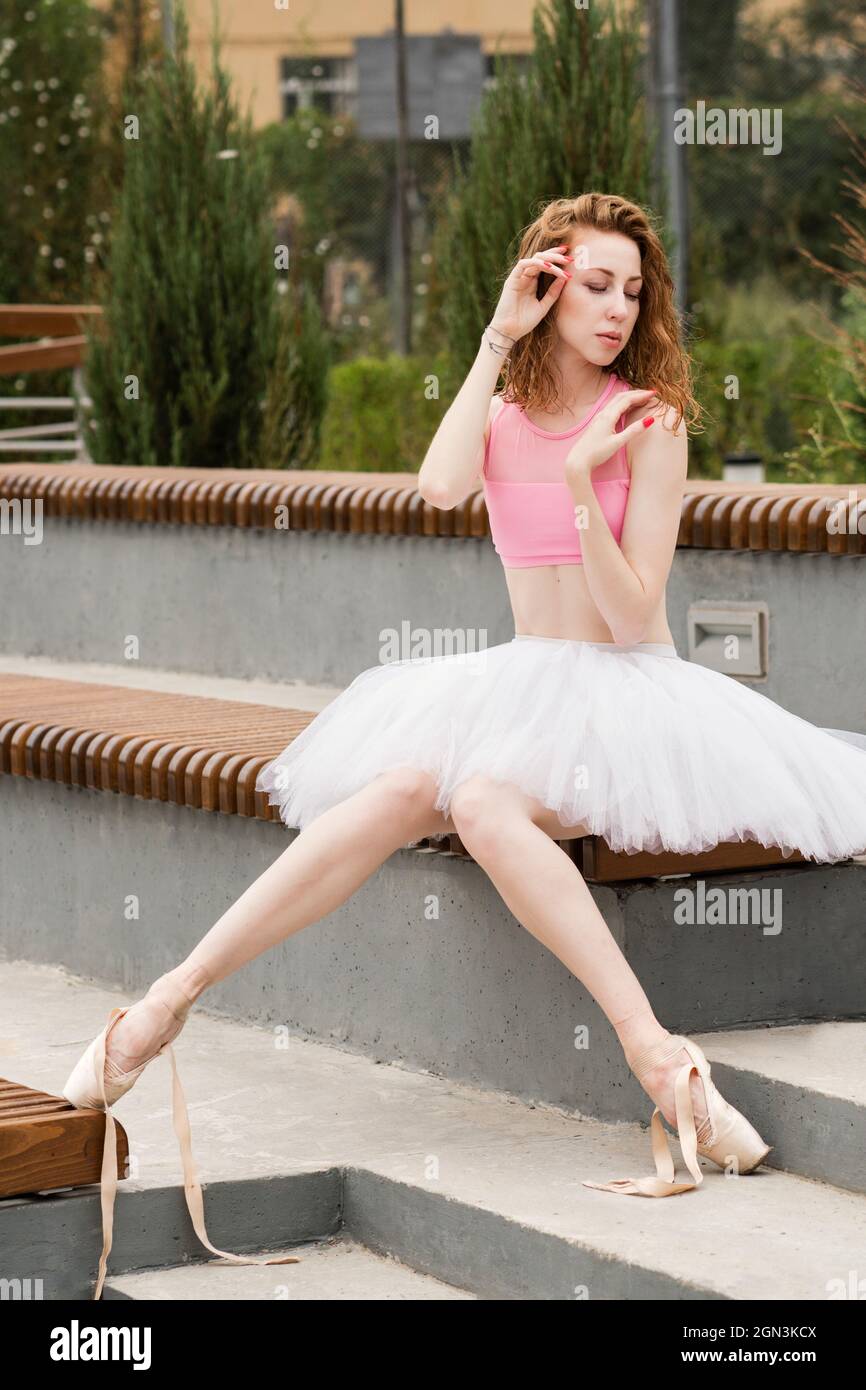 Ballet dancer girl sits on park bench. Ballerina has pointe shoes on feet.  Dance shoes are not tied Stock Photo - Alamy