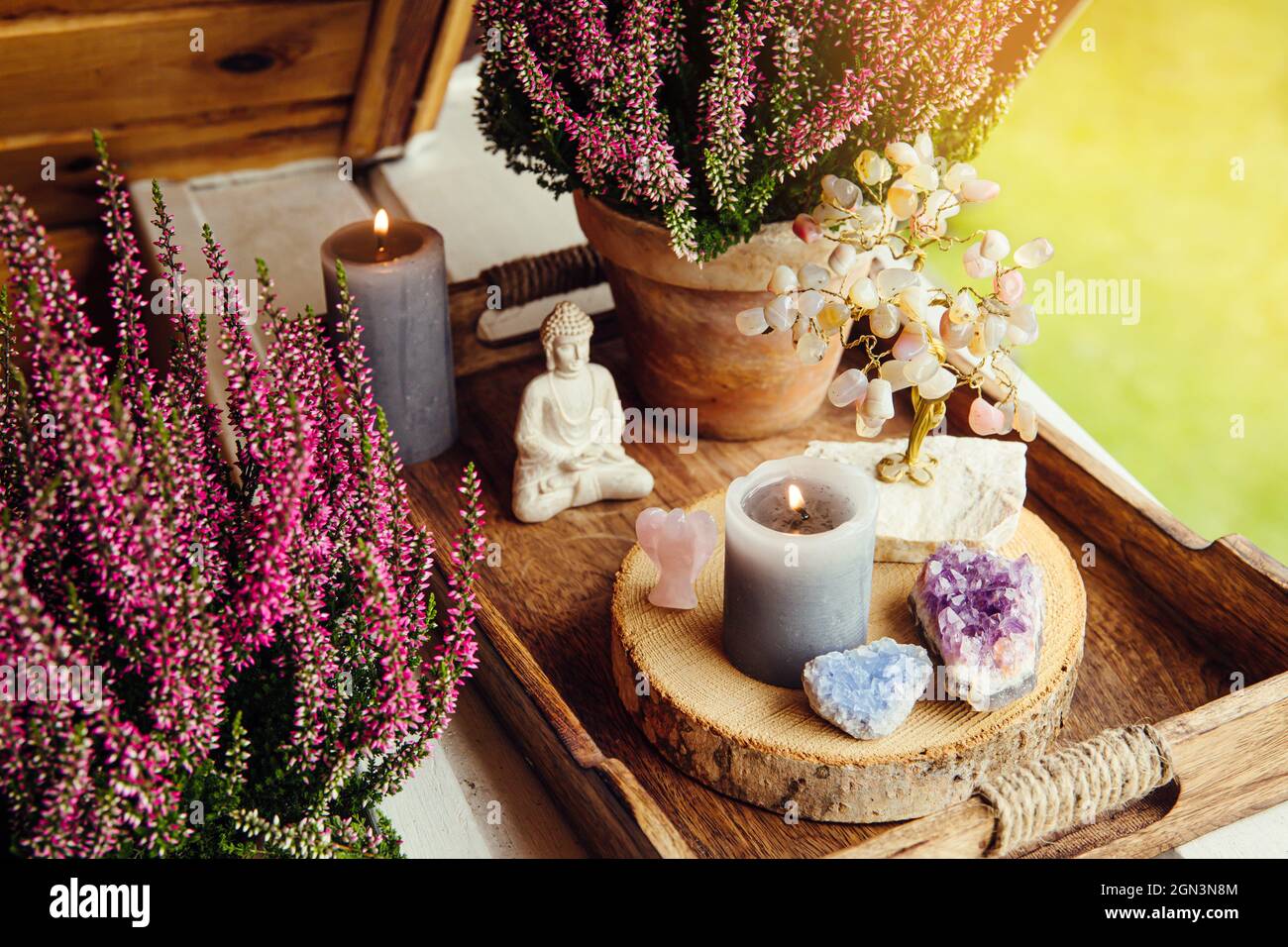 Spiritual home balcony decor with pink heather flowers, candlelight flame, crystal geodes, crystal wire tree and small Buddha figurine. Cute autumn sp Stock Photo