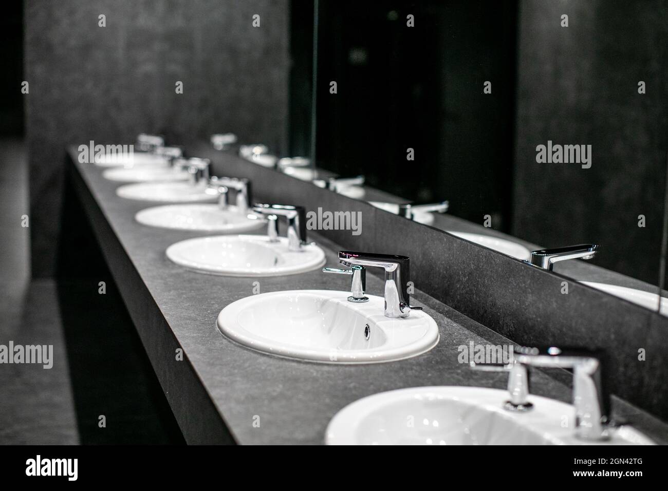 Faucets with washbasin in public restroom in gray colors Stock Photo