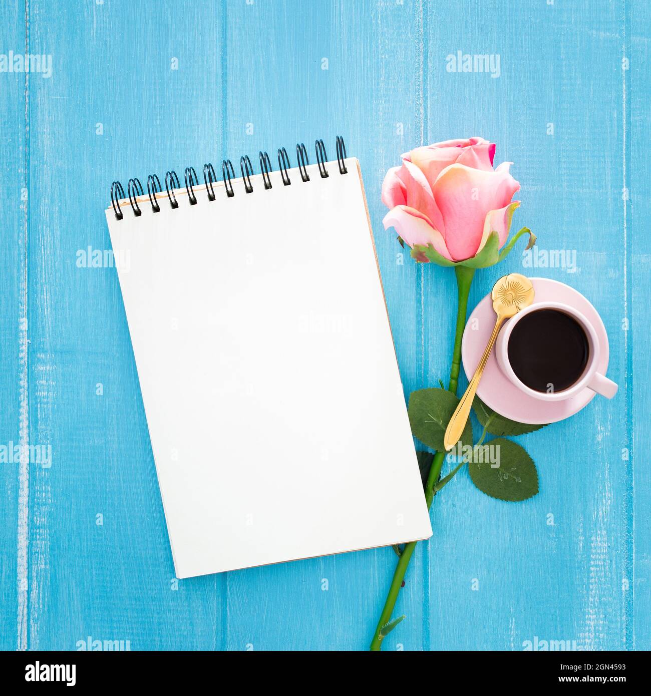 Blank notebook with space for text, a cup of coffee and a pink rose on a blue surface Stock Photo