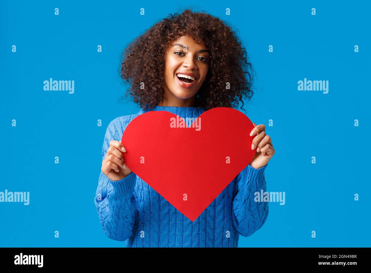 Lovely and cute african-american pretty woman with afro haircut, holding valentines day card, big heart and smiling, express love and affection Stock Photo
