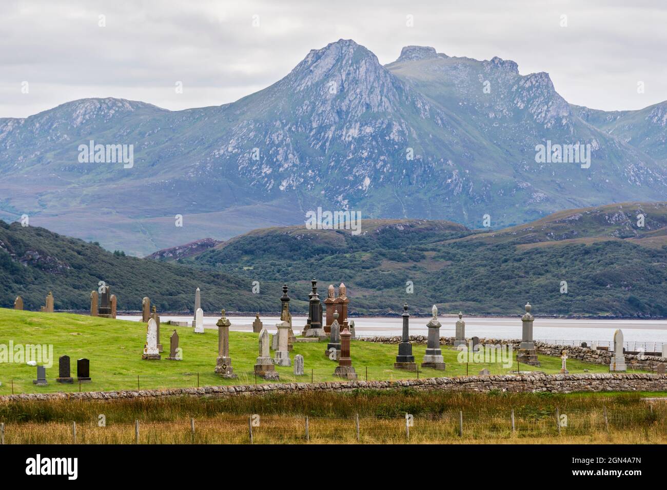 The jagged peaks of Ben Loyal rise behind the low wooded hills beside the Kyle of Tongue and the Melness cemetery on the NC500, northern Scotland. Stock Photo