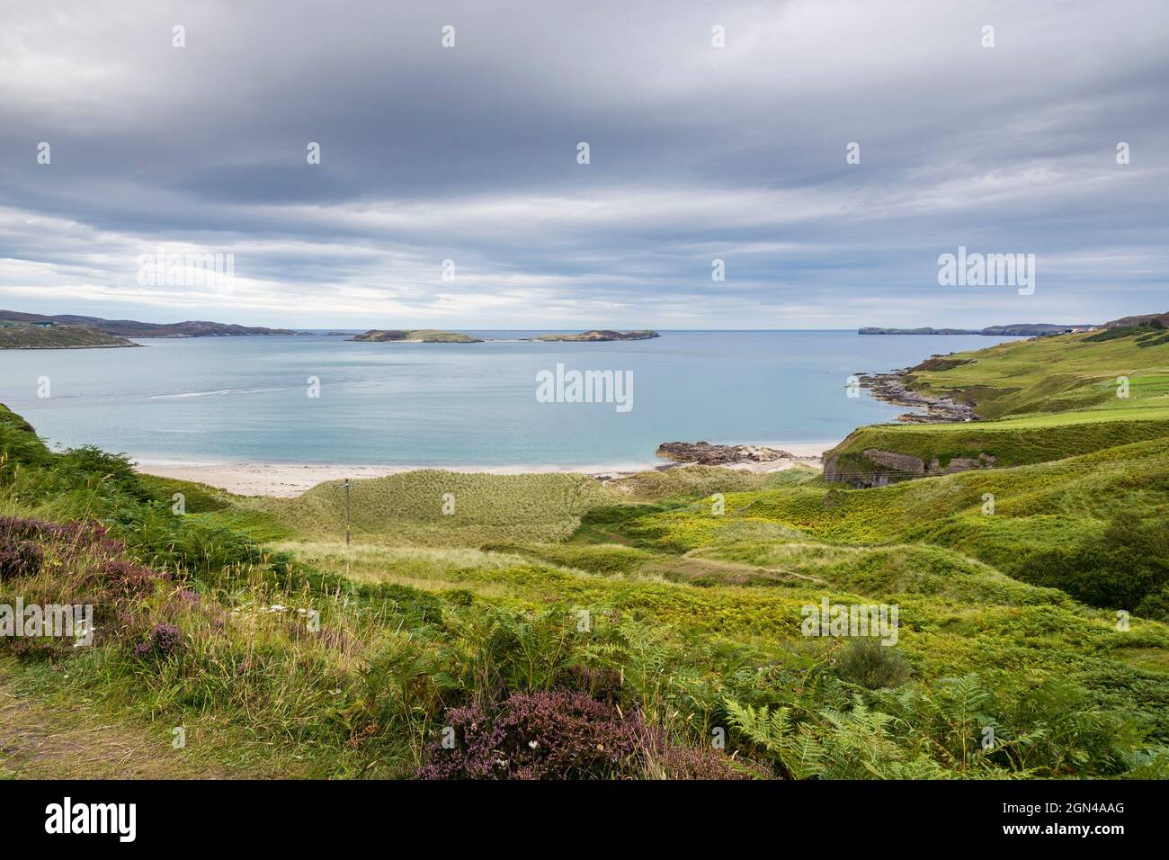 Grassy slopes lead down to dunes and the sandy Coldbackie beach, on the shore of Tongue Bay on the NC500 route in northern Scotland, on a cloudy day. Stock Photo