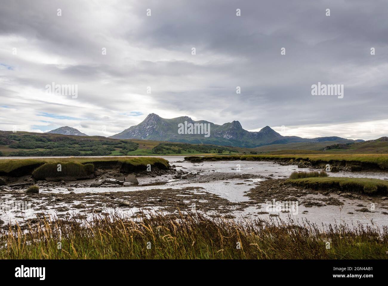 The jagged peaks of Ben Loyal rise beyond the intertidal muddy foreshore of the  Kyle of Tongue near the NC500, northern Scotland, on  a cloudy day. Stock Photo