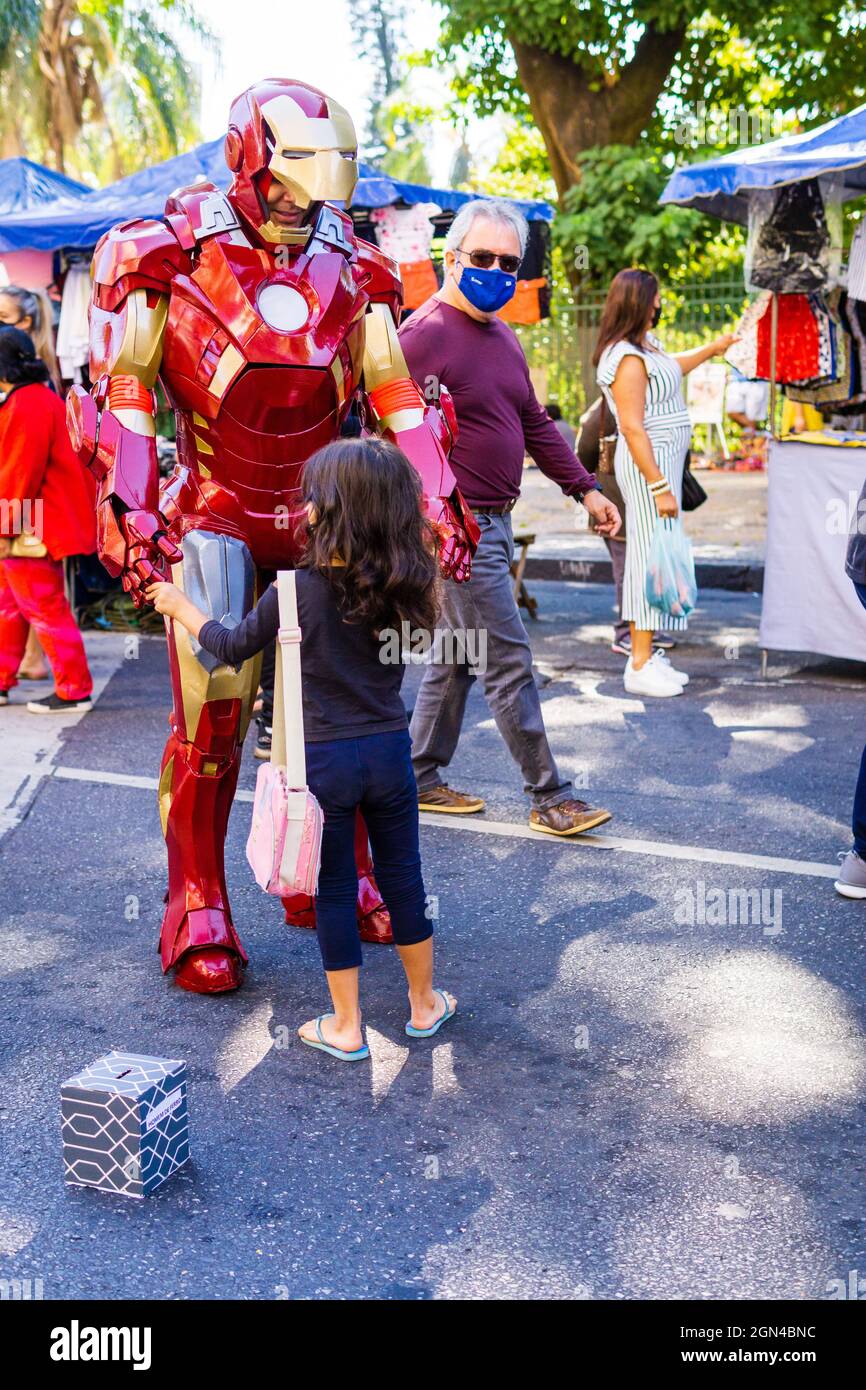 A little girl holding hands with a street performer dressed in an Iron Man costume at the Belo Horizonte Hippie Fair in Brazil. Stock Photo