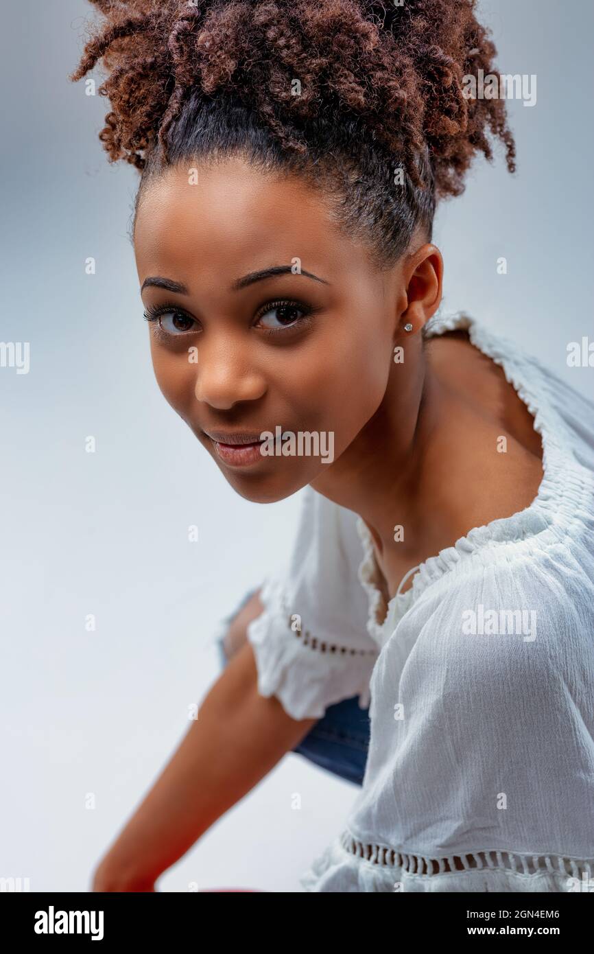 Beautiful young woman with a calm expression looking up at the camera as she crouches down on her haunches in a cropped studio portrait Stock Photo