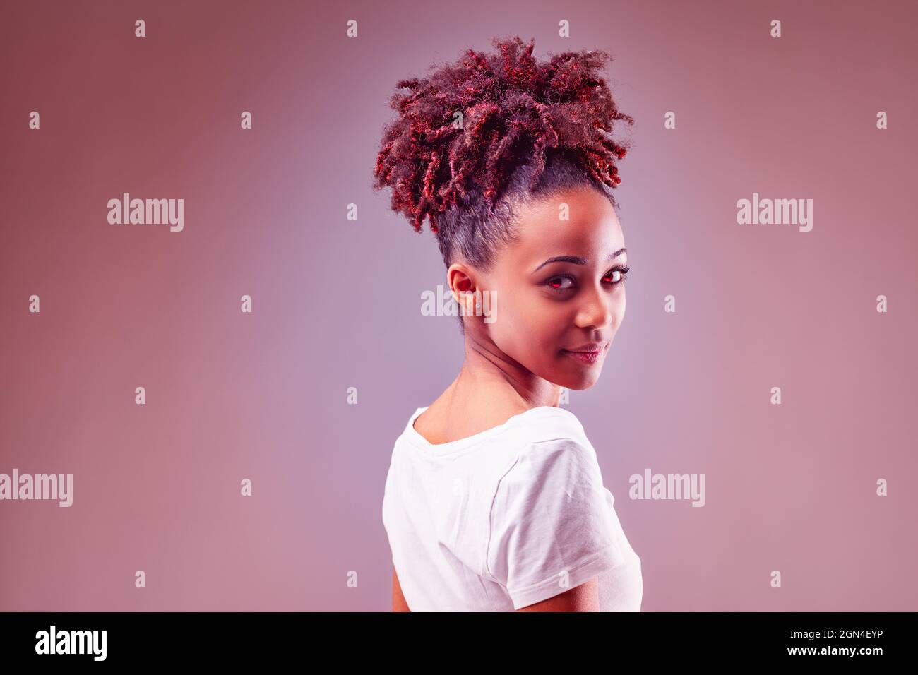 Artisitic red toned portrait of an attractive young Black woman with her curly hair as embers piled on top of her head turning to looking back over he Stock Photo
