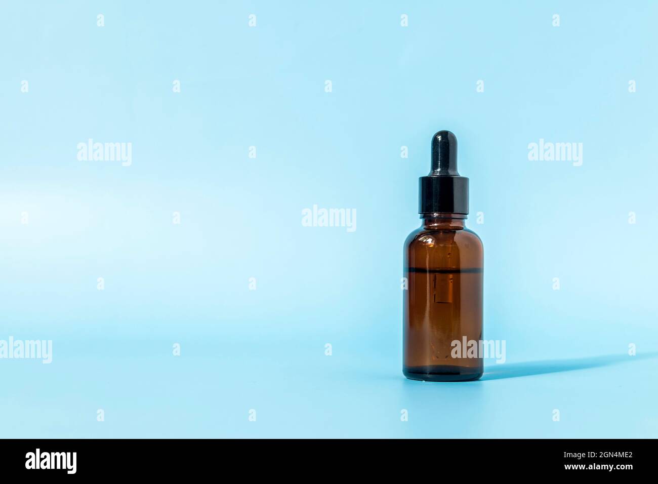 Glass dropper bottle made of brown glass on a blue background casts a shadow. Front view with copy space. Mockup of a cosmetic product. Serum for skin Stock Photo