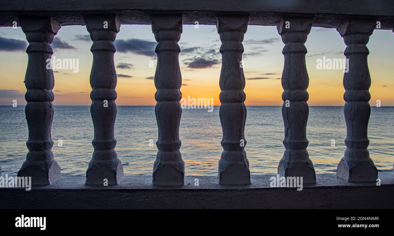 A colorful sunset seen through balustrades on a beachfront balcony. Rincon, Puerto Rico. Stock Photo