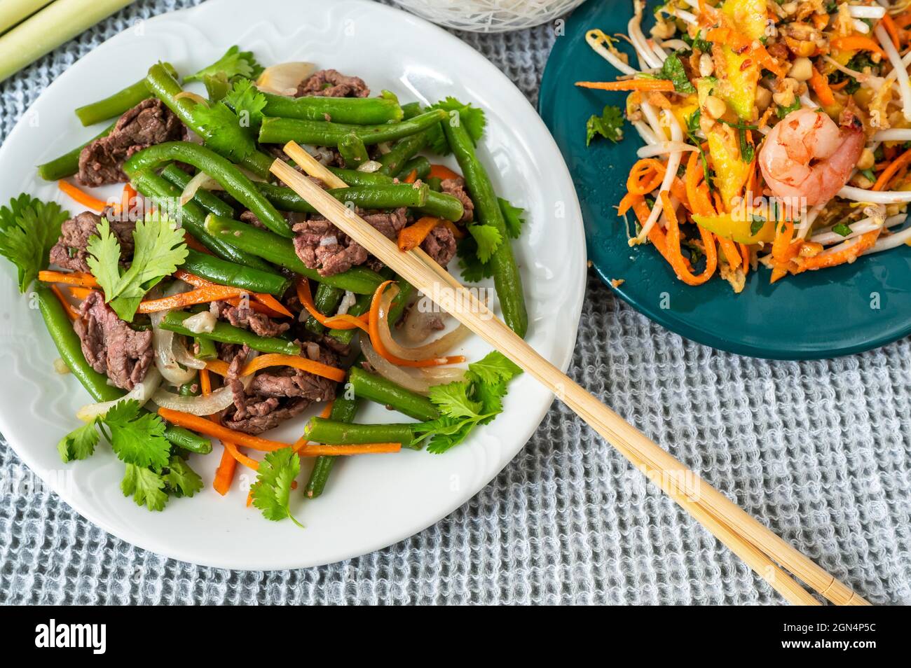 Two plates on table with traditional vietnamese meal and chopstick. Fried beef with green bean, carrot and onion and mango salad with shrimp. Stock Photo