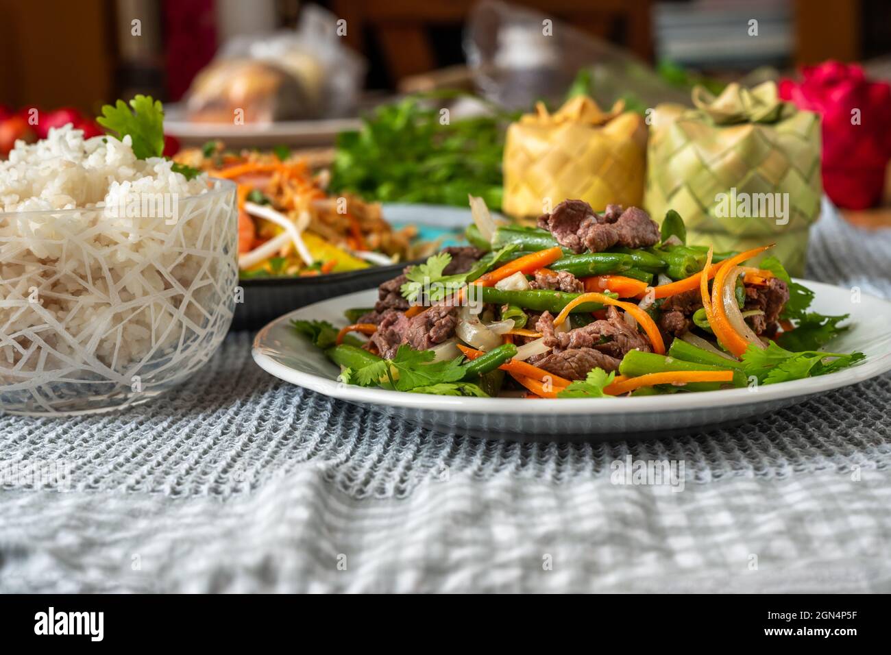 Vietnamese meal on plate, fried beef with green bean and carrot, rice in bowl, mango salad and bamboo box on table. Stock Photo
