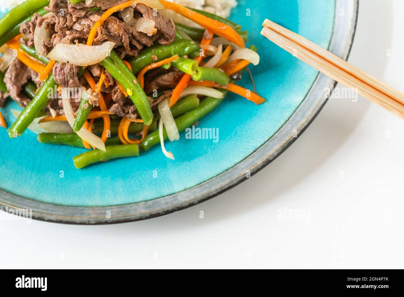Part of blue plate with sliced roasted beef with green beans, carrot and onion, chopstick on white background. Vietnamese traditional food. Stock Photo
