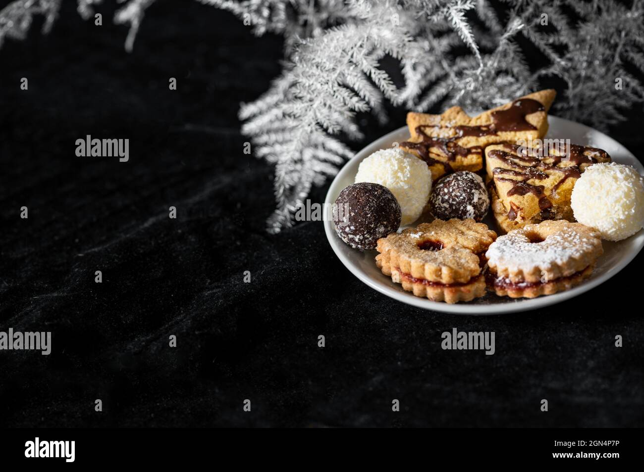 Pile of christmas cookies on white plate on black velvet background with white bracken twig. Stock Photo
