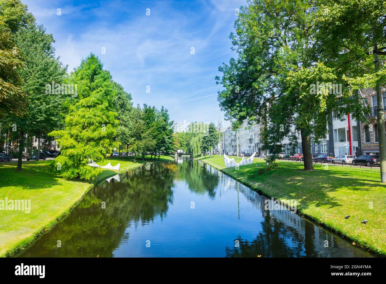 Urban park leafy trees idyllically reflected in calm water of canal running through city under large leafy tree Stock Photo