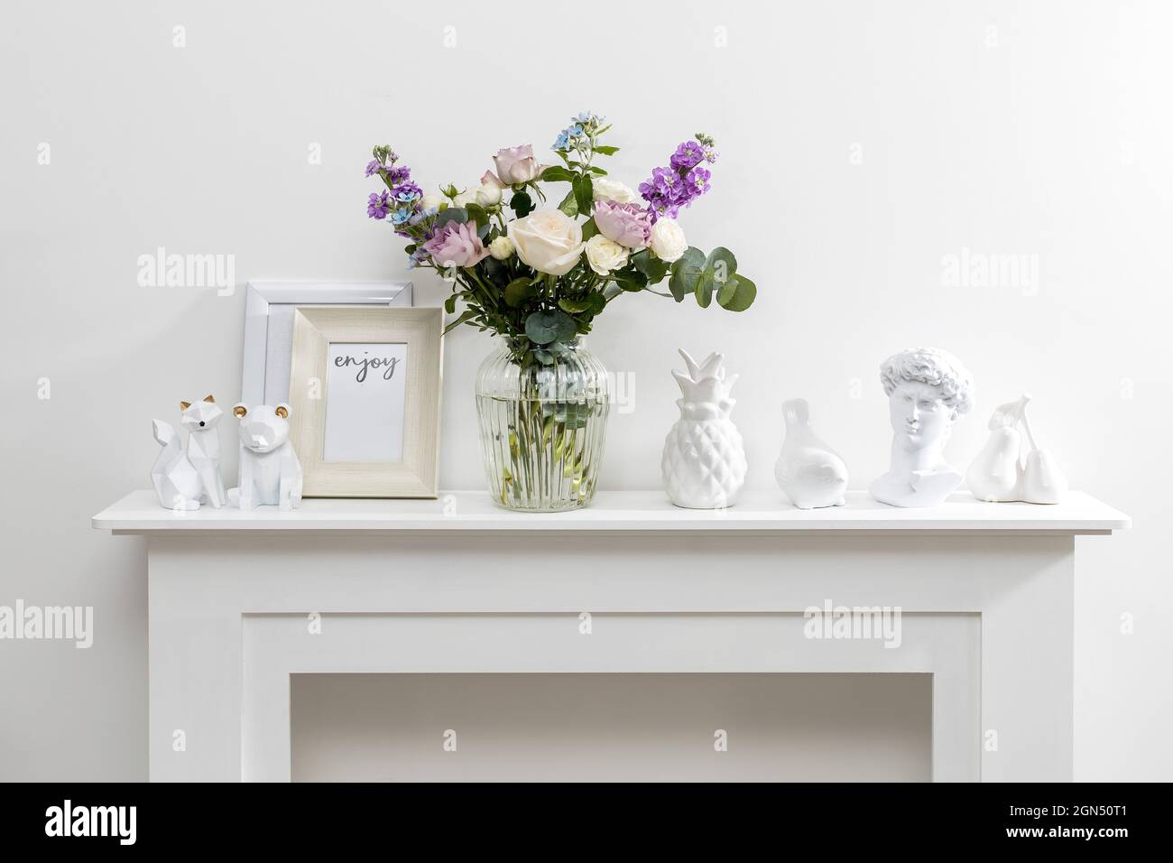 Bouquet of hackelia velutina, purple and white roses, small tea roses, matthiola incana and blue iris in glass vase is on the white coffee table . Gre Stock Photo