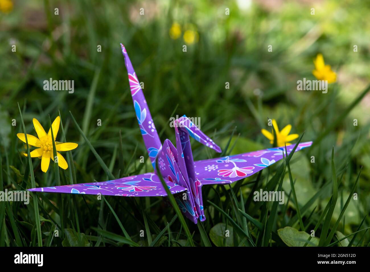 Close-up of a paper origami crane sitting on grass between blossoming early bloomers symbolizing spring time, a fresh start and hope Stock Photo