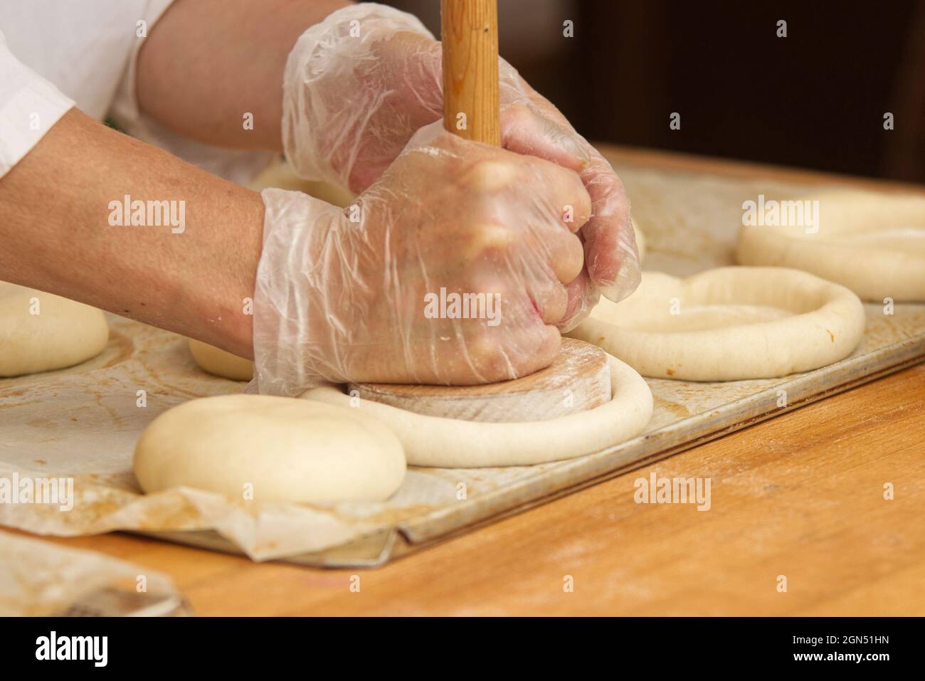 The woman in the picture is making filled pies. Hands in protective gloves holding the tool press dough to get the proper shape of pie. Work in the ba Stock Photo