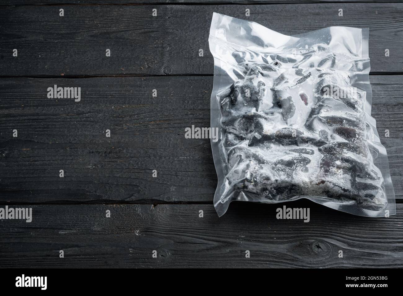 Vacuum packed whole shell mussels frozen, on black wooden table