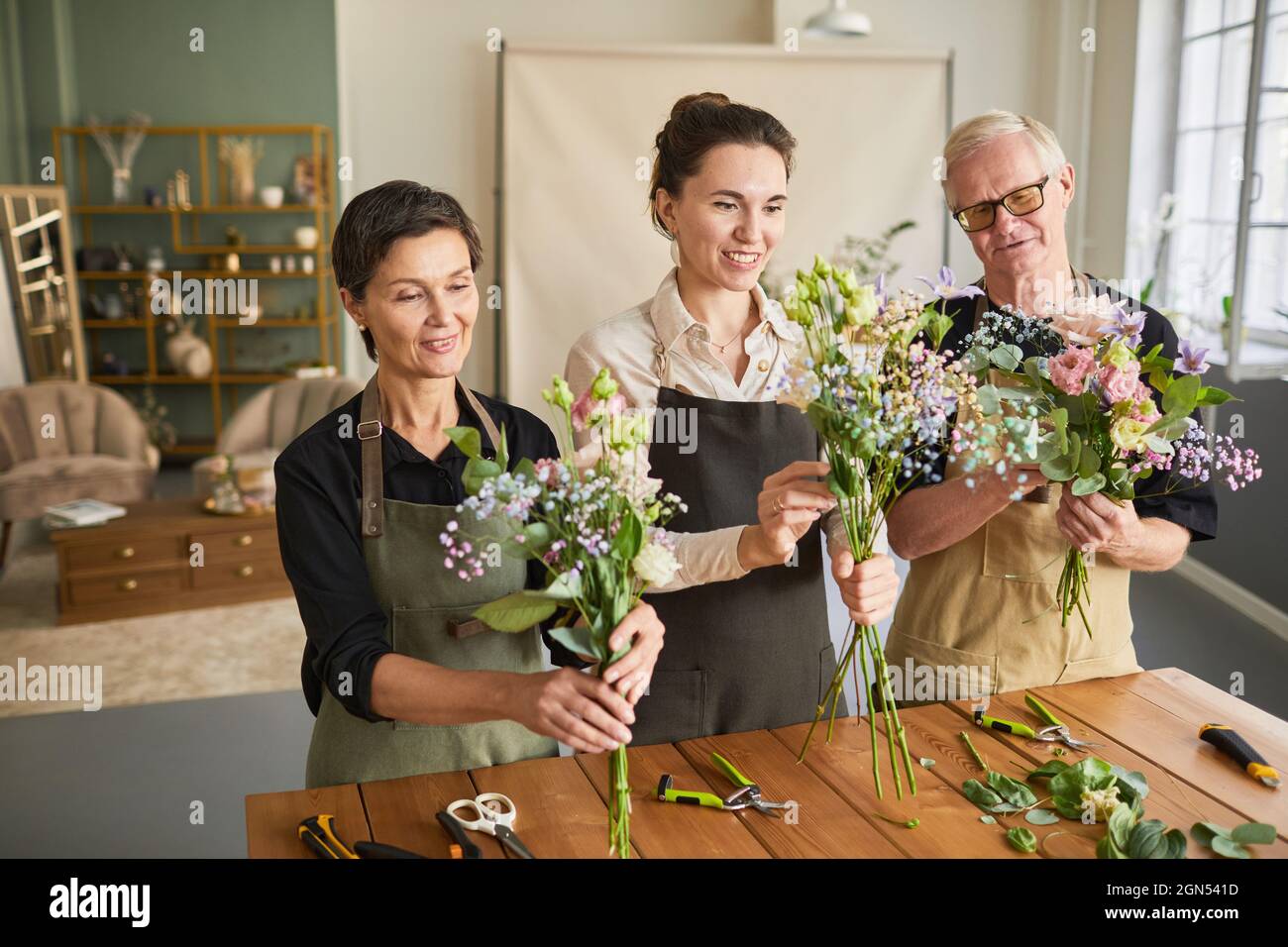 Waist up portrait of three florists arraigning flower compositions while working in cozy workshop Stock Photo