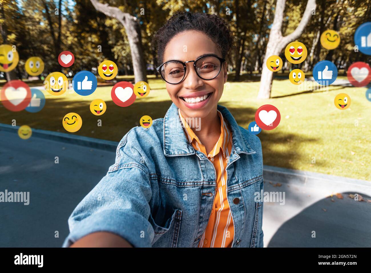 Happy millennial afro american lady in casual, glasses makes selfie in park for social networks and blog Stock Photo