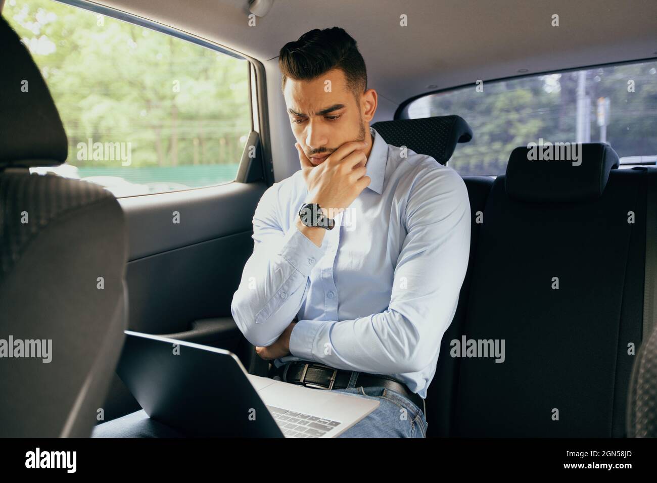Pensive middle-eastern businessman working at car, using laptop Stock Photo