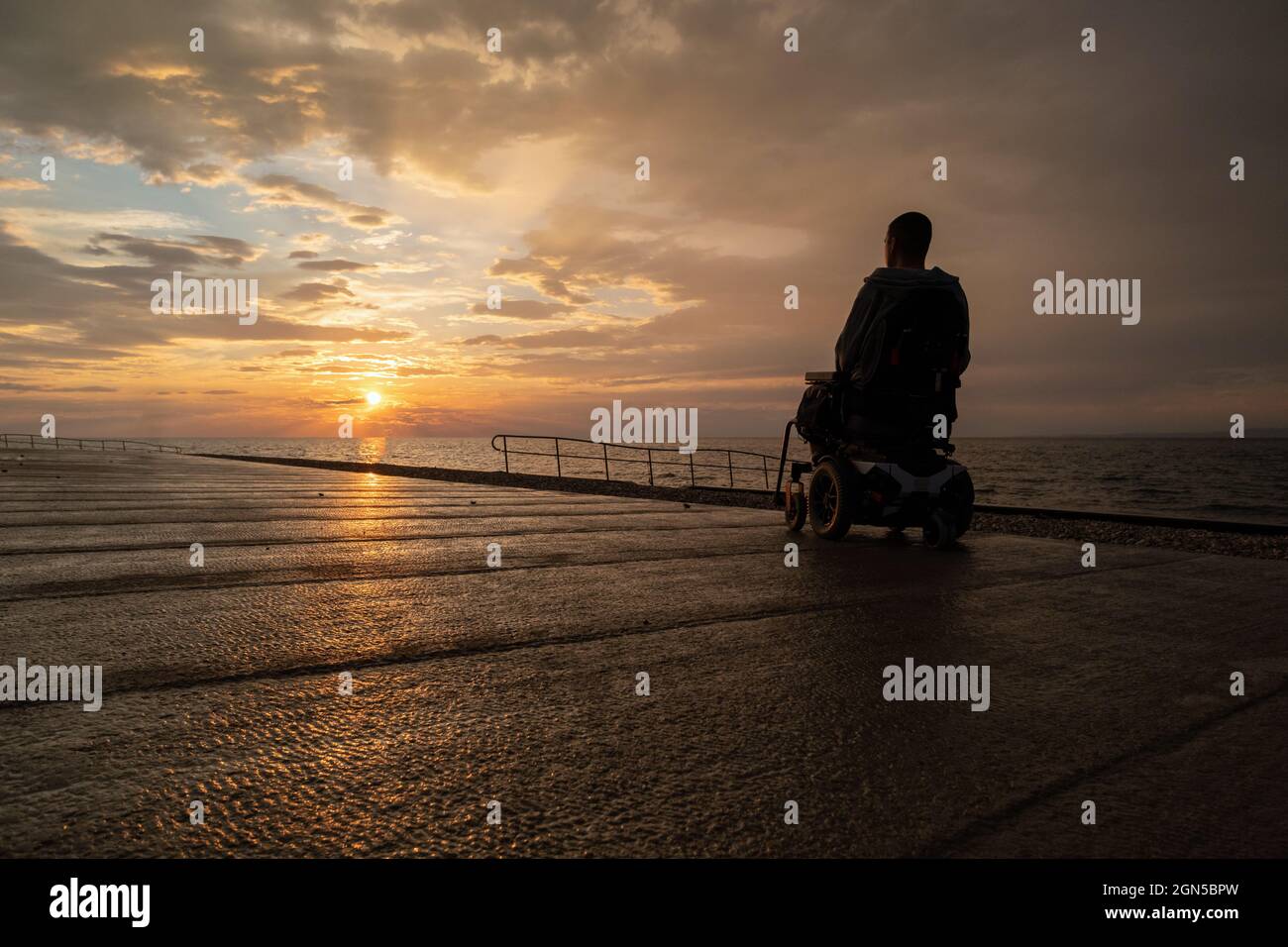 Disabled person in a wheelchair at sunset looking at sea Stock Photo ...