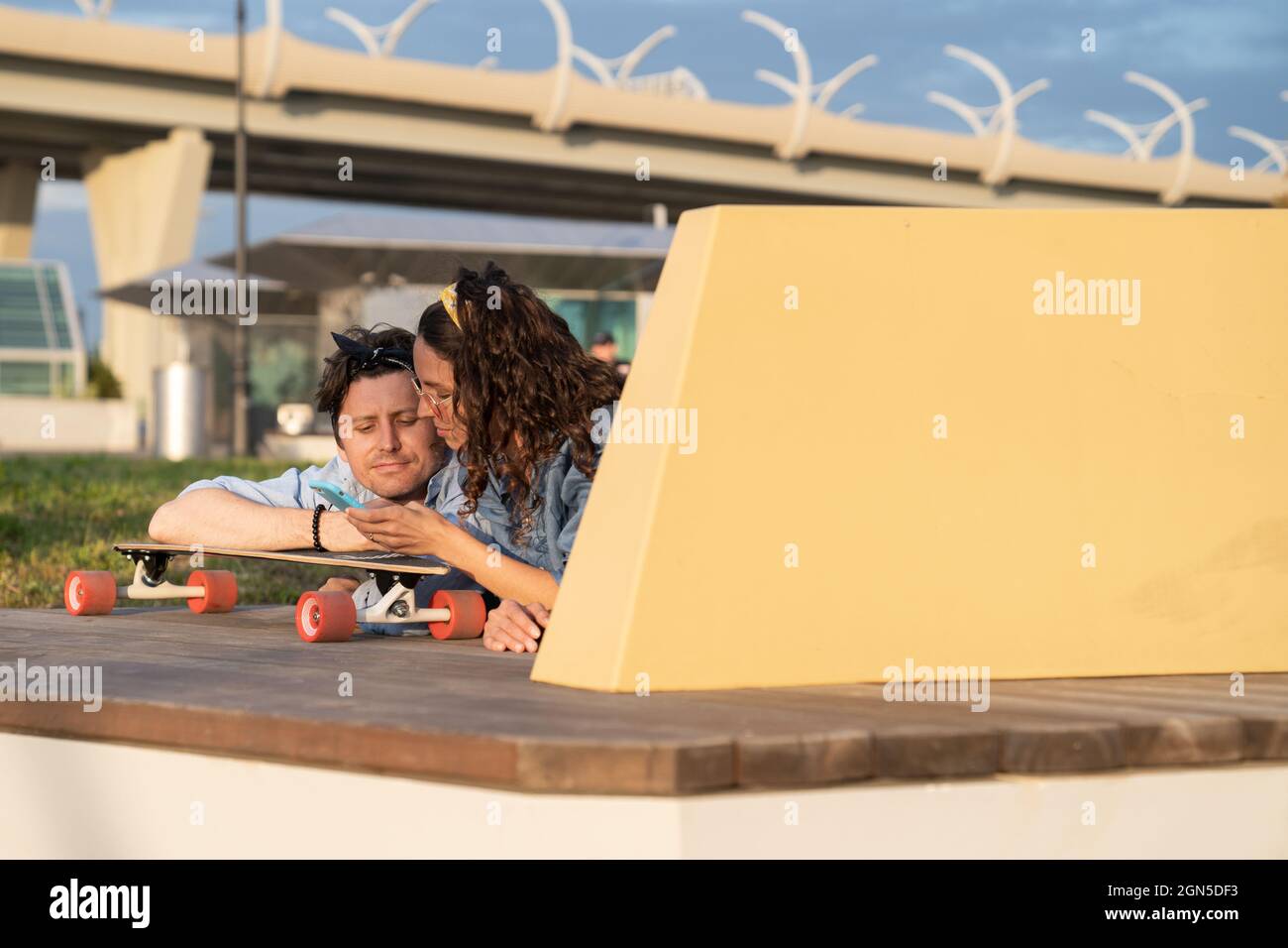 Trendy couple use smartphone relaxing together lying on longboard outdoors browse websites, shopping Stock Photo