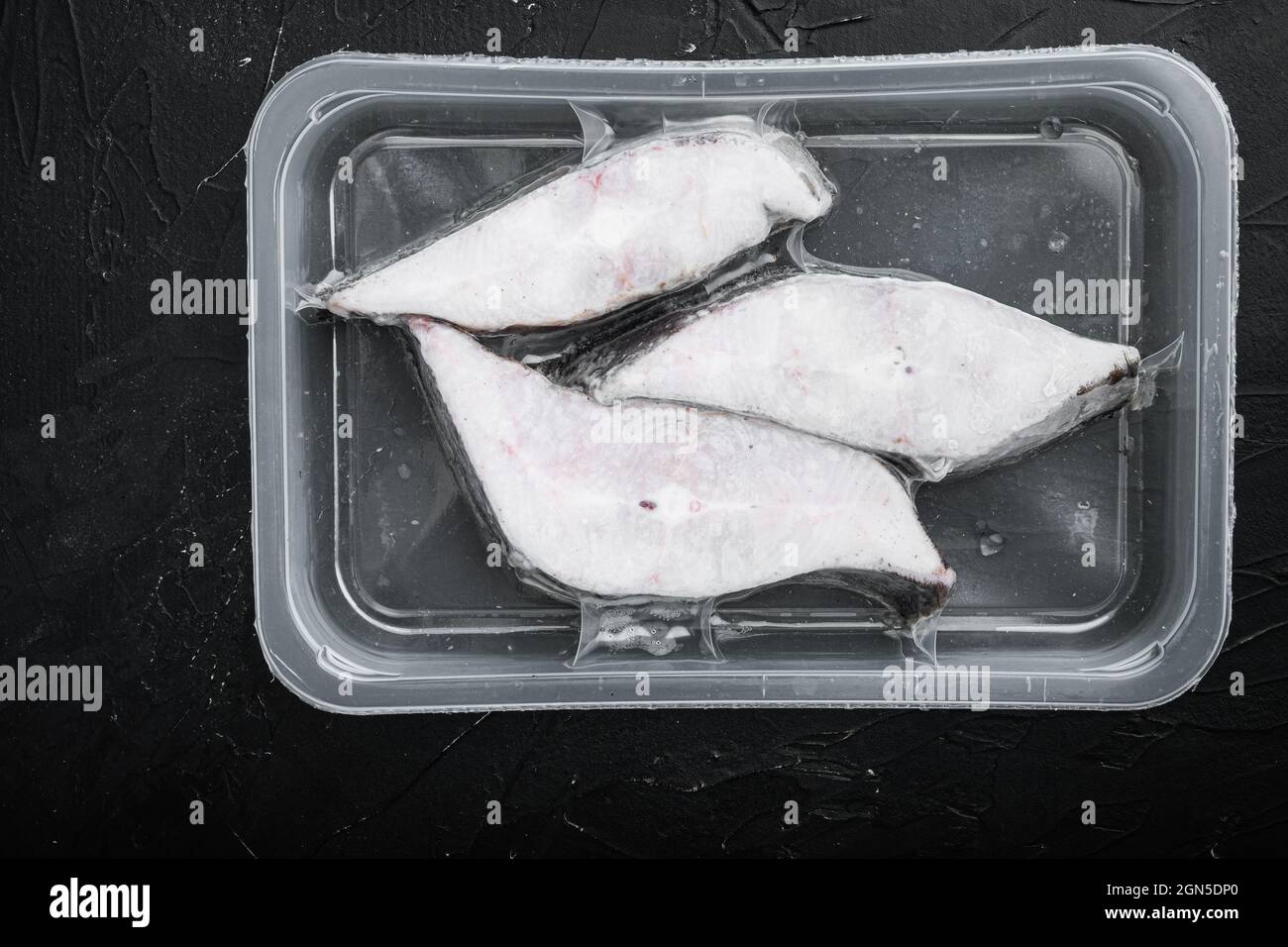 Raw fillets frozen halibut airtight vacuum pack set, on black dark