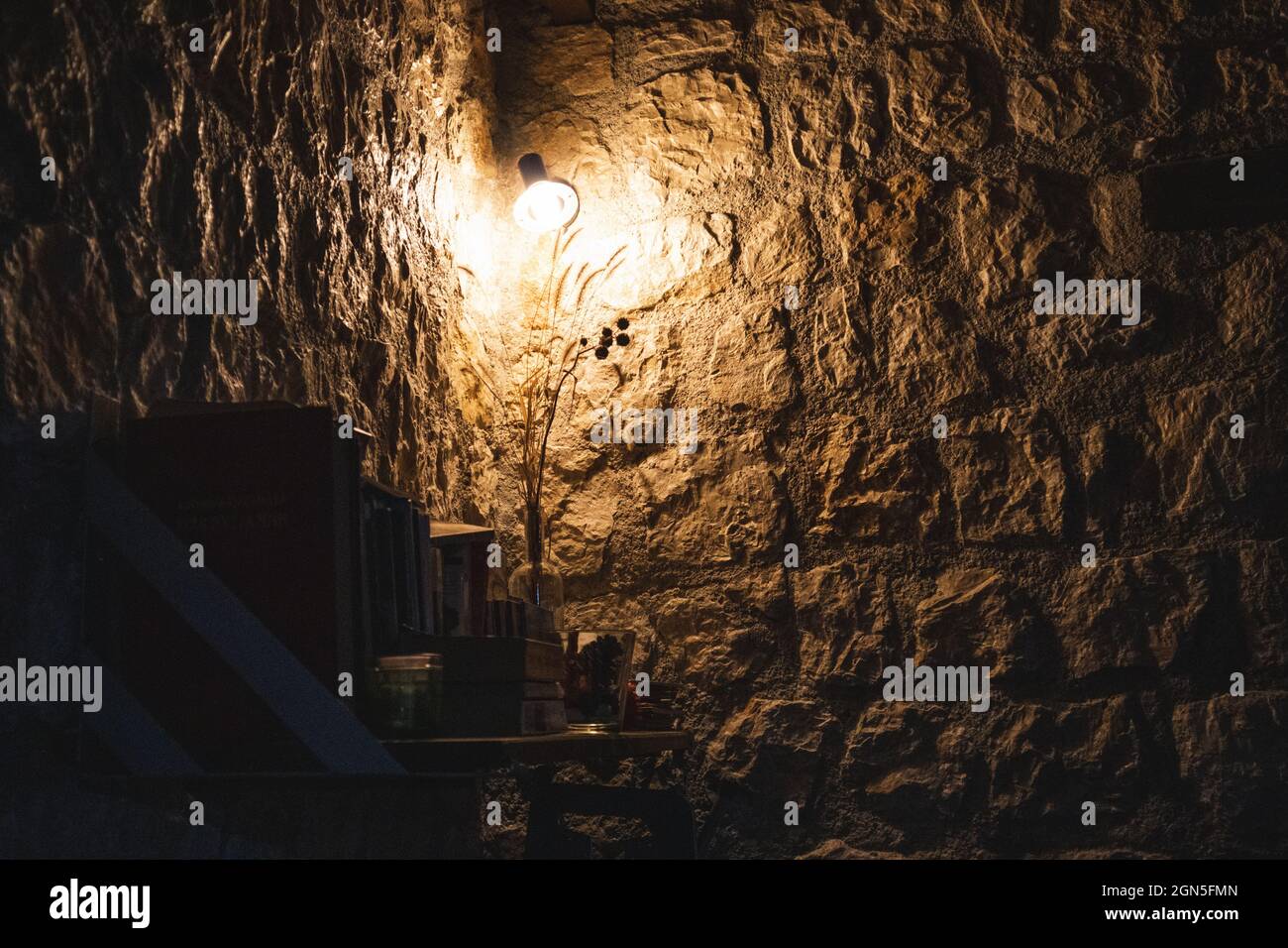 Warm cozy lamp in corner on bookshelf in dark room with stone walls. Greek guest house evening rest area, decor interior elements Stock Photo