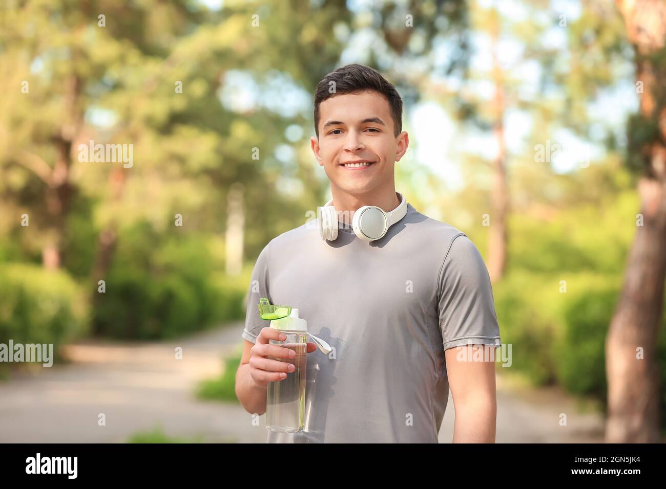 Sporty young man with bottle of water and headphones in park Stock ...