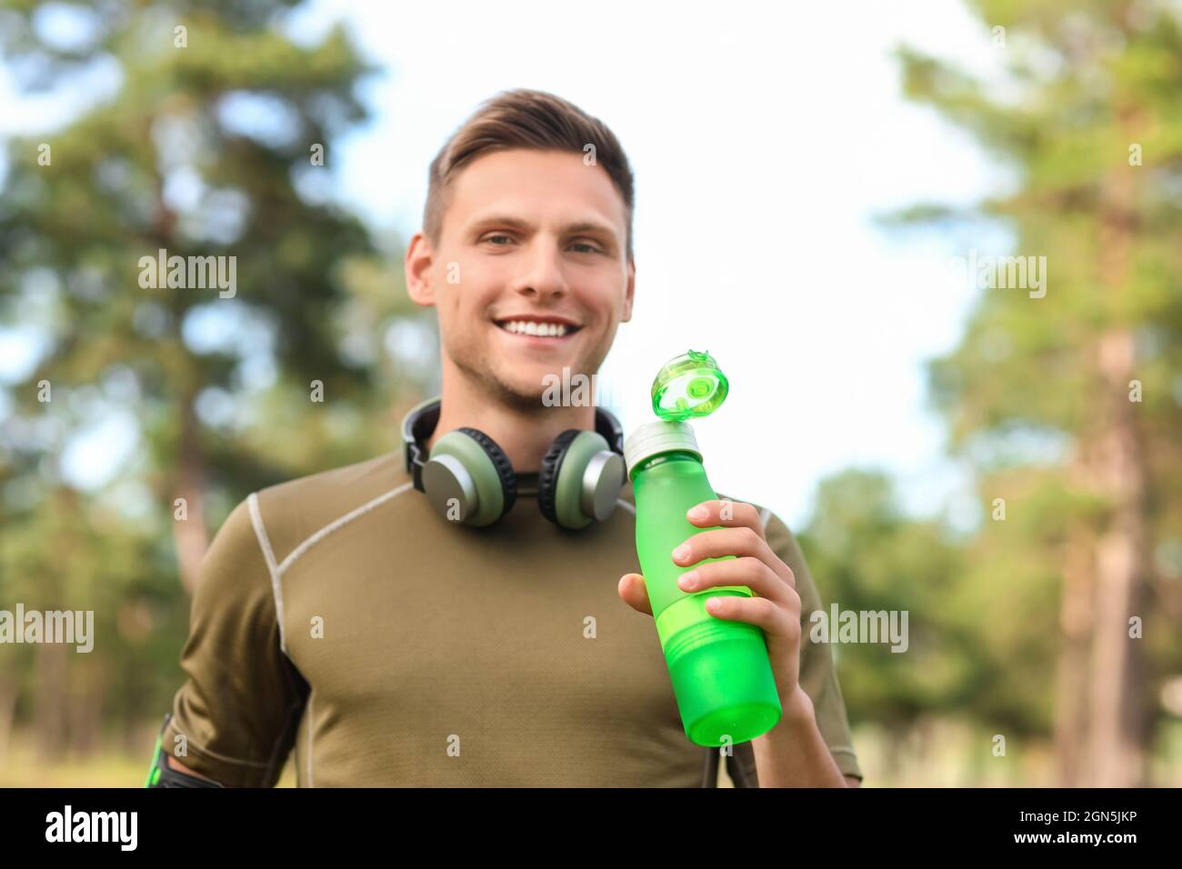 Sporty young man with bottle of water and headphones in park Stock ...