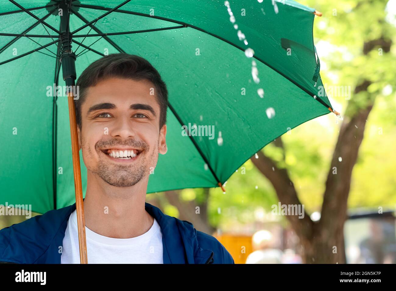 Handsome young man with umbrella in park on rainy day Stock Photo - Alamy