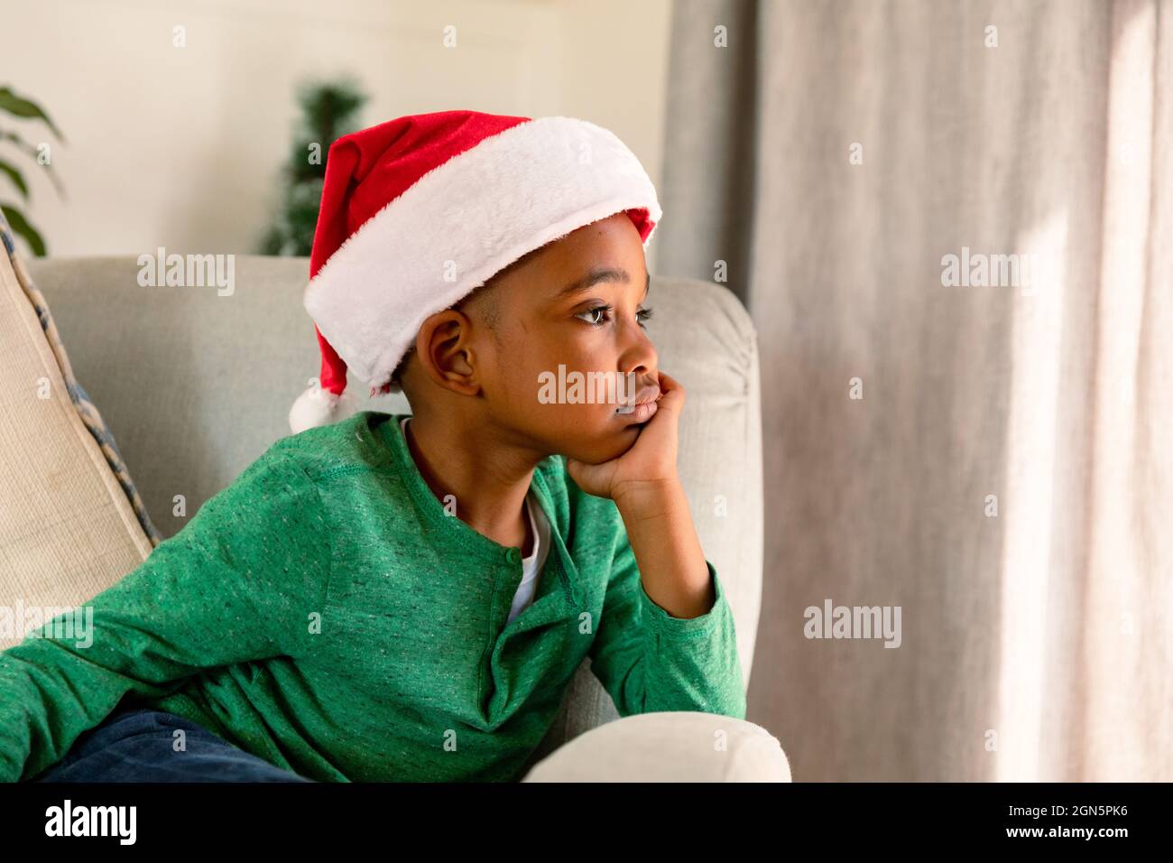 Thoughtful african american boy wearing santa hat and sitting in armchair at christmas time Stock Photo